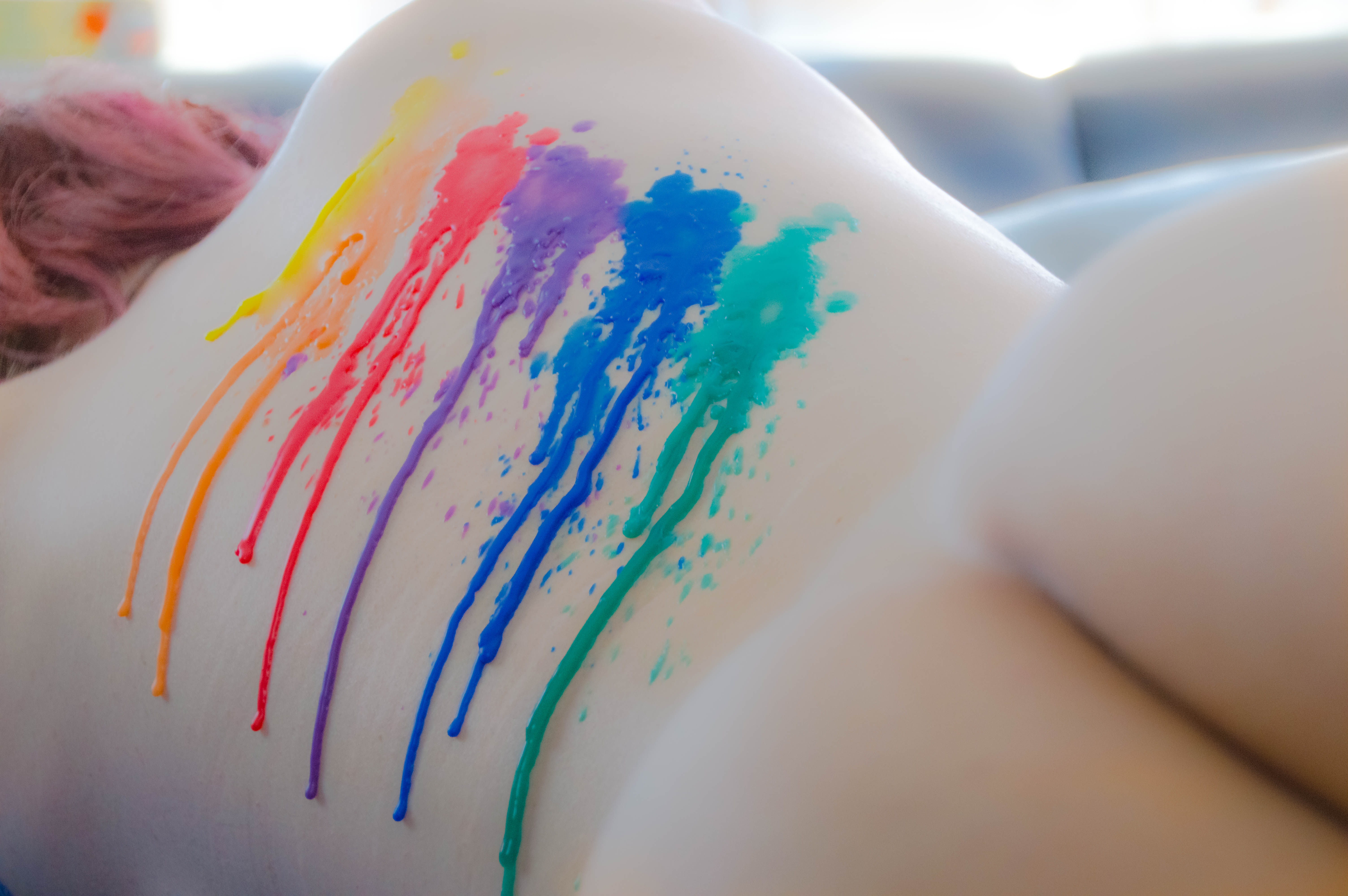 Der Rücken einer nackten Frau, beträufelt mit Wachs in den Farben des Regenbogens.