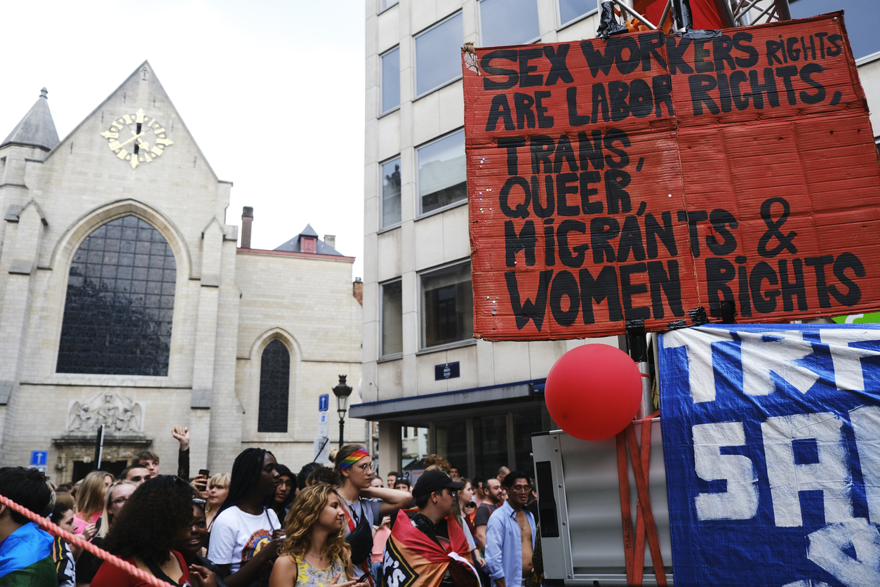 Die Menschen nehmen an der jährlichen belgischen LGBT Pride Parade teil, auf einem Schild steht "Sexworker rights are labor rights, trans, queer, migrants & women rights", auf deutsch "Rechte von SexarbeiterInnen sind Arbeitsrechte, Trans, Queer, MigrantInnen und Frauenrechte"